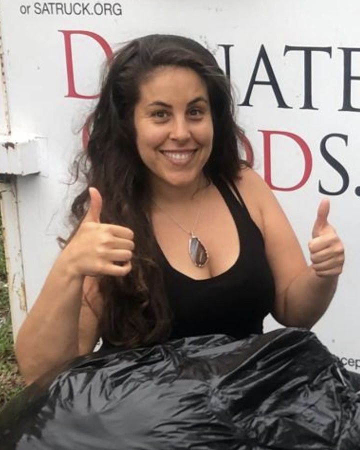 Marlee smiling with two thumbs up beside bags of donations